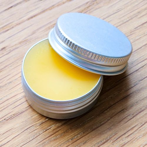 Unlabelled metal tin containing yellow dog skin balm on wooden surface